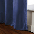 A draped navy blue curtain with a subtle sheen flowing onto a rich brown hardwood floor next to a white window frame
