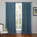 An interior room with elegant blue linen window curtains framing a sunlit view of green trees and grass, beside a classic white armchair and a botanical lemon print