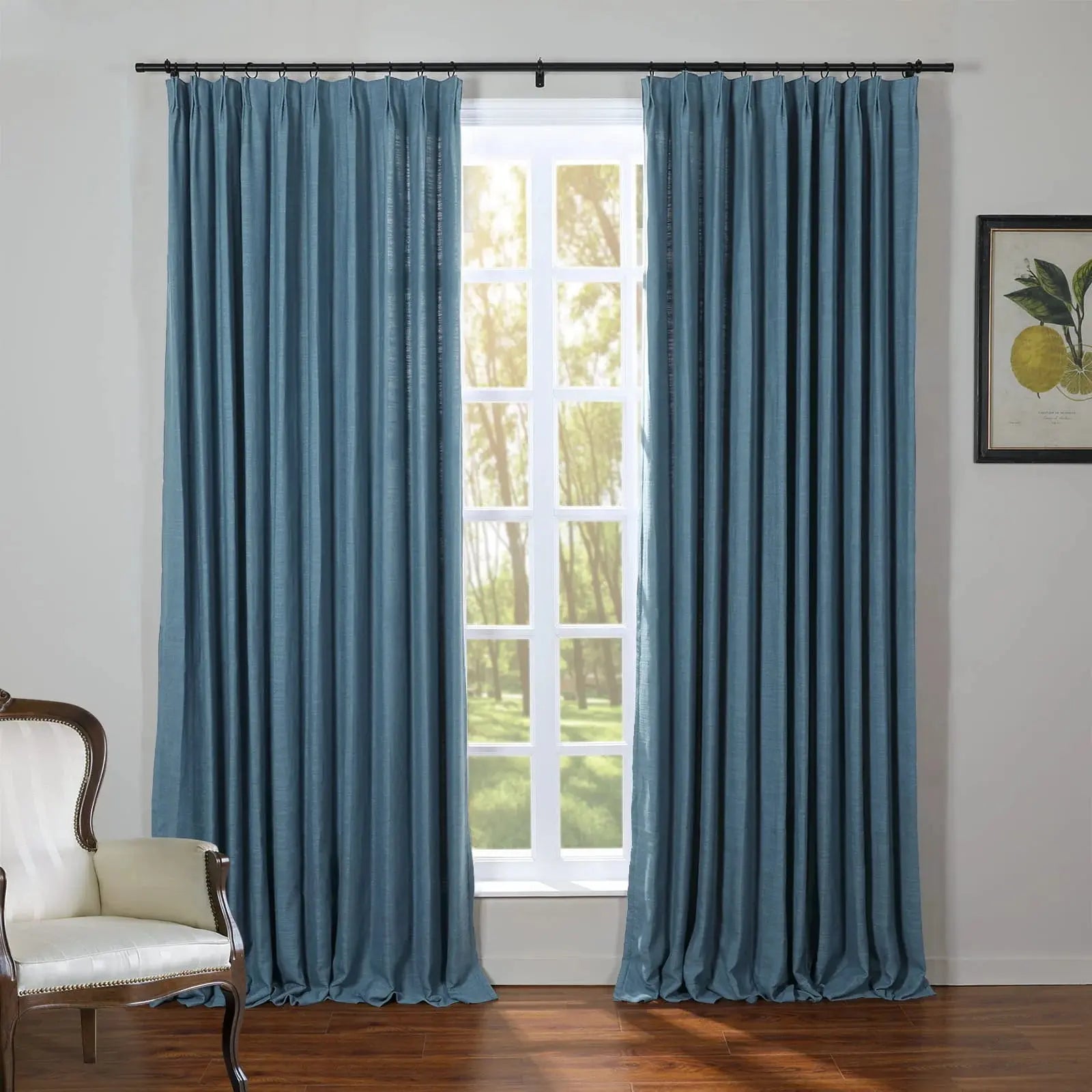 An interior room with elegant blue linen window curtains framing a sunlit view of green trees and grass, beside a classic white armchair and a botanical lemon print