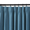 A teal blue pleated curtain made of textured fabric hangs from a black curtain rod with visible black rings