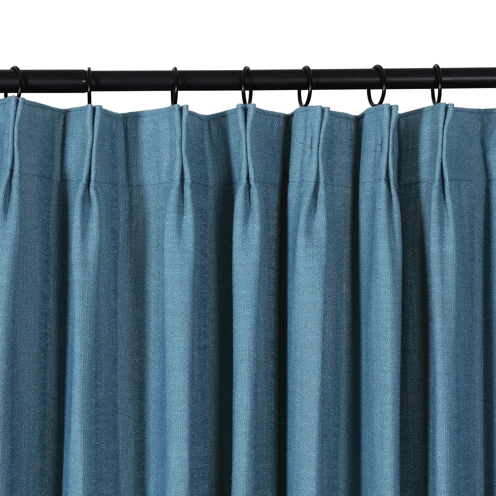 A teal blue pleated curtain made of textured fabric hangs from a black curtain rod with visible black rings