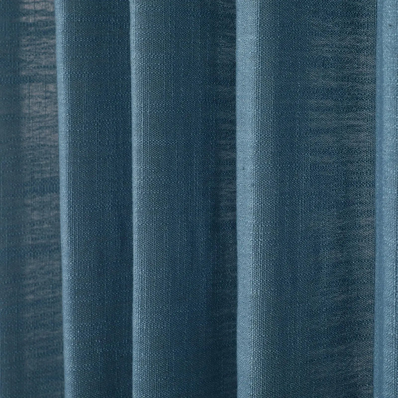 Photograph of deep teal blue woven fabric curtains showing prominent vertical folds and subtle light variations across its textured surface