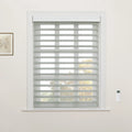 A bright interior room with a window featuring grey and white striped zebra Blinds, a white ornate window frame, a botanical print on the left wall, and a white remote control mounted on the right
