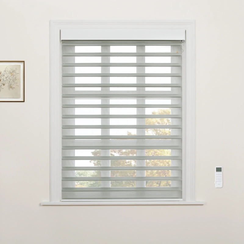 A bright interior room with a window featuring grey and white striped zebra Blinds, a white ornate window frame, a botanical print on the left wall, and a white remote control mounted on the right