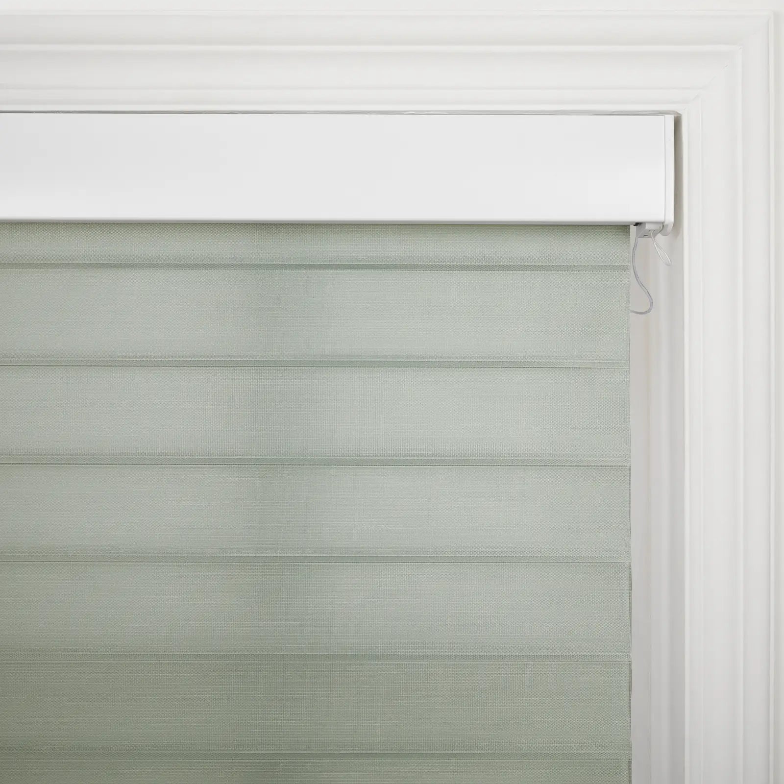 Modern window Blind with alternating sage green opaque and sheer horizontal fabric stripes, framed by white decorative trim and a valance, featuring a control cord