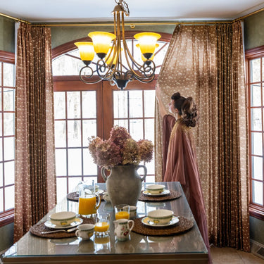 MS. MAVERICK MUSE x TWOPAGES Dusty Clay floral curtains surrounding a formal dining room bay window with a set table and chandelier