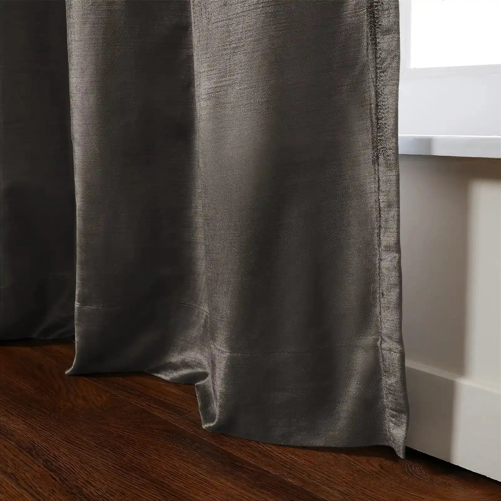 Photograph of a textured charcoal grey curtain panel with subtle sheen draped beside a white window sill, extending to rich brown hardwood flooring