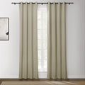 Beige grommet top curtains on a black rod in a bright room with an abstract white and black framed artwork and a view of outdoor greenery through the window above a natural fiber rug