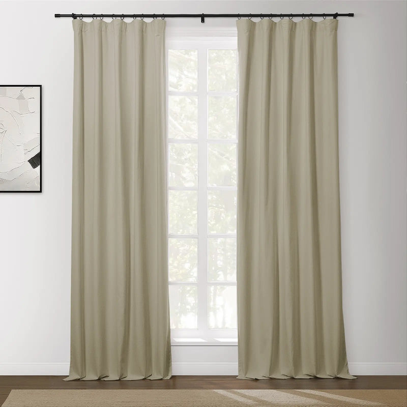 Beige blackout curtains with a black ring top rod frame a white gridded window showing lush green trees