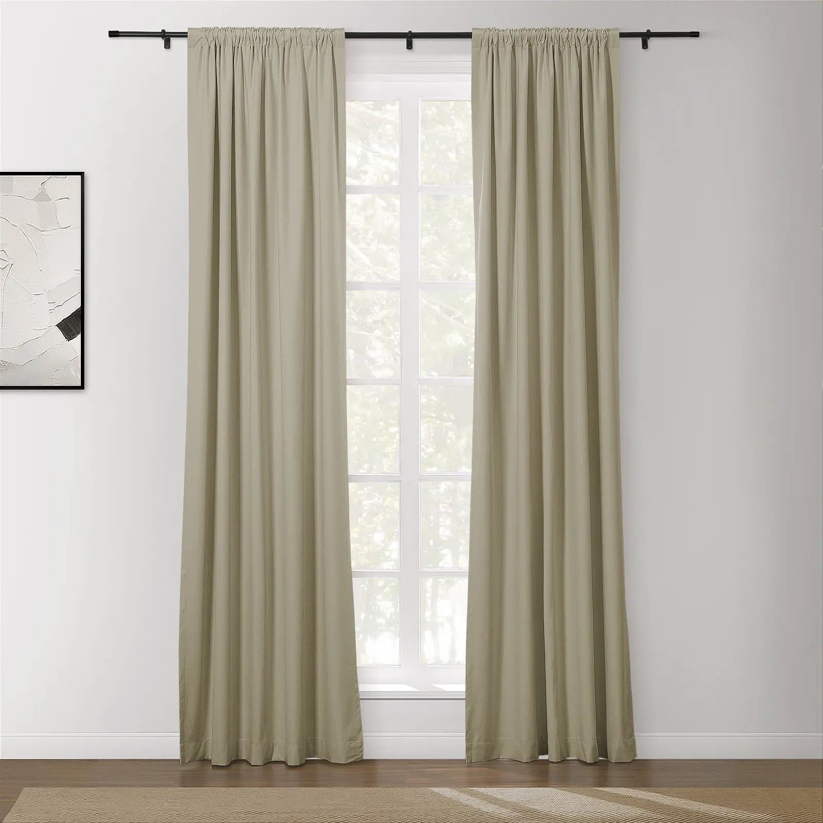 A pair of pleated beige curtains on a black rod over a multi-pane window with visible green foliage in a modern room featuring abstract black and white framed artwork and a textured tan rug on a wooden floor