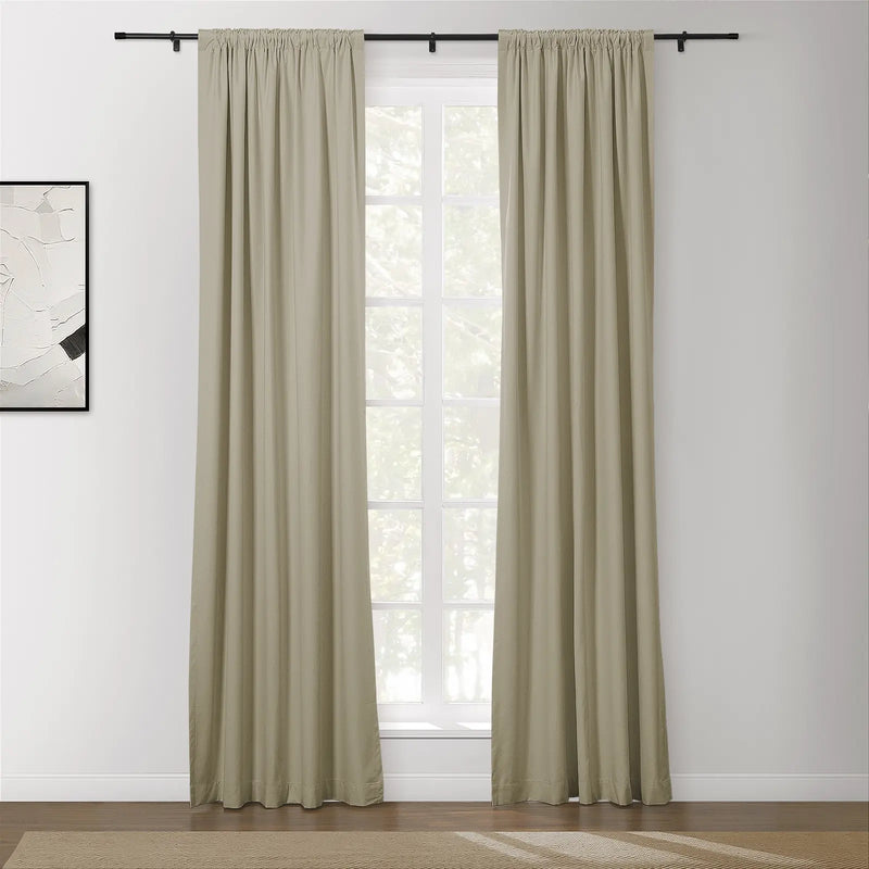 A pair of pleated beige curtains on a black rod over a multi-pane window with visible green foliage in a modern room featuring abstract black and white framed artwork and a textured tan rug on a wooden floor