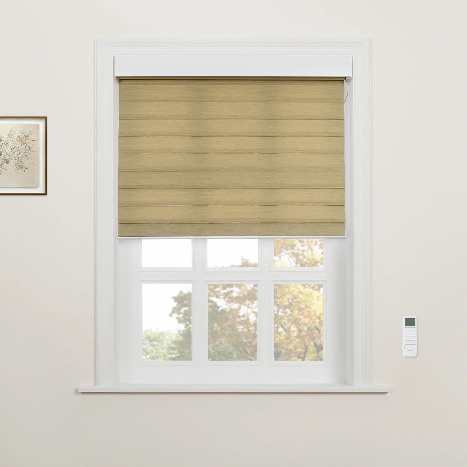 Tan horizontally striped motorized window Blind in a white framed window revealing autumn trees outside, with a wall-mounted remote and a framed botanical print