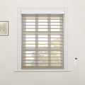 White-trimmed window featuring tan and sheer striped zebra Blinds, a white remote control on the right wall, a framed botanical print on the left, and autumn trees visible through the window
