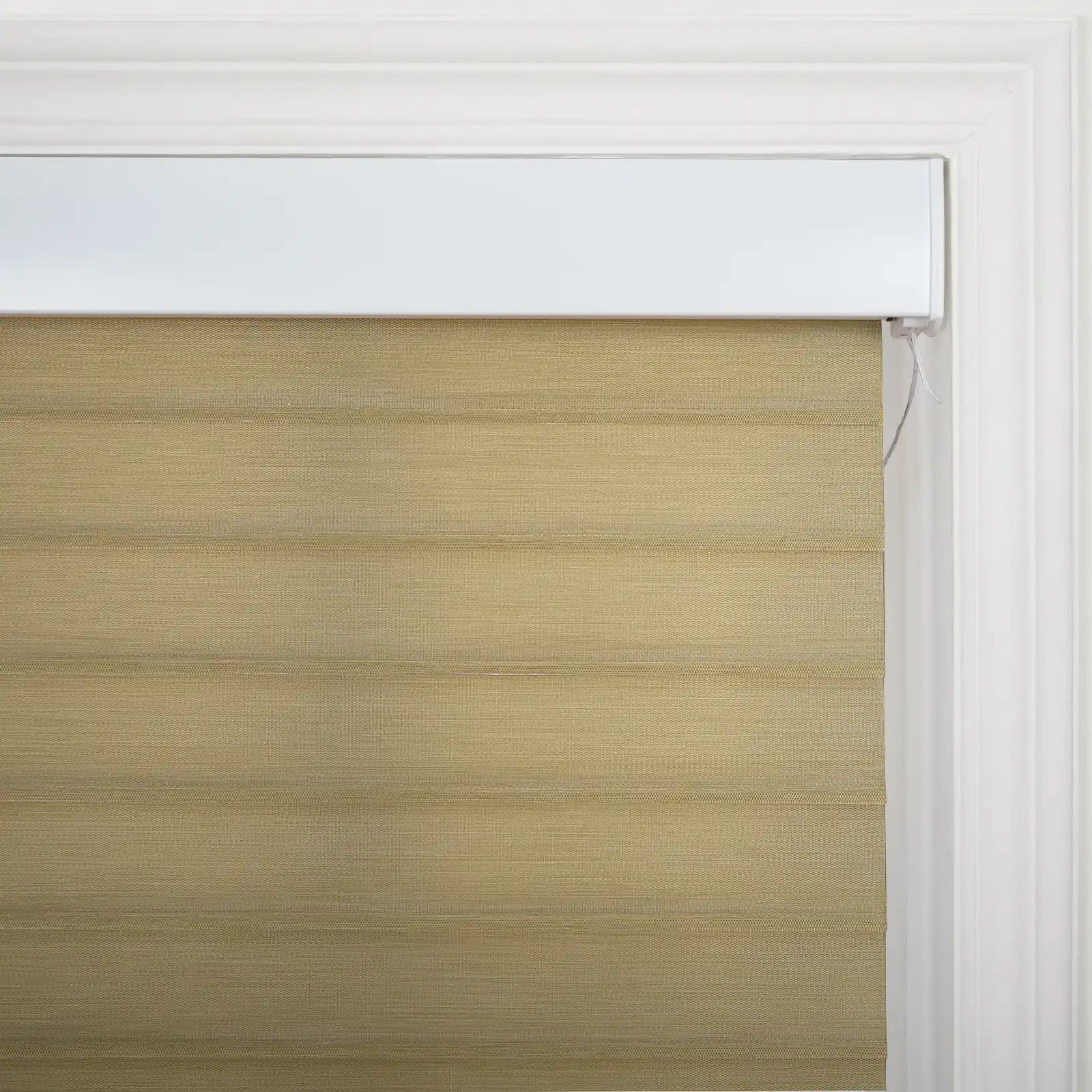 Tan woven Roman Blind with horizontal folds and a white headrail, showing a pull cord against a white decorative window frame