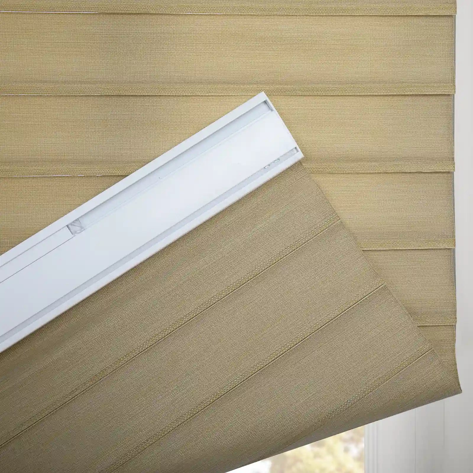 Photograph of a textured beige Roman window Blind with visible white headrail installation hardware and horizontal fabric folds against an interior window with subtle outdoor greenery