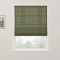 A Roman blind in olive green with a subtle grey floral and grid pattern covers the top of a white-framed window, with blurred green trees visible outside and a framed landscape painting on the adjacent wall