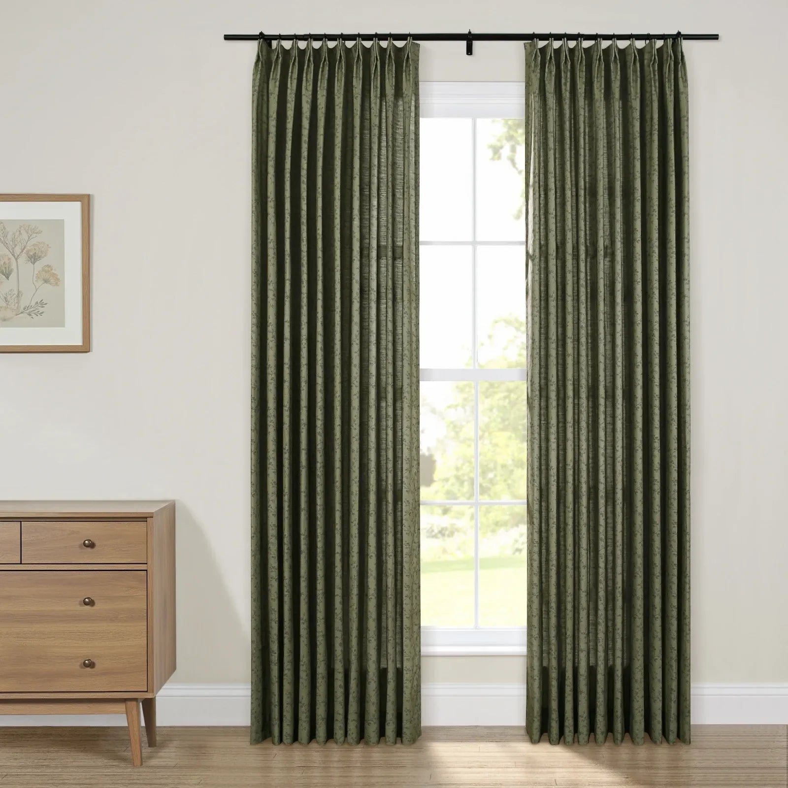 Pleated dark green patterned curtains on a black rod adorn a bright window in a contemporary room featuring a light wood mid-century modern dresser with brass pulls and a framed botanical print artwork