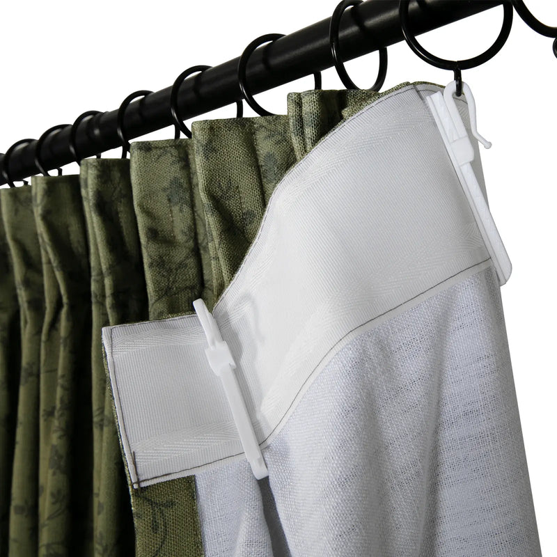 Close-up of olive green pinch pleat curtains featuring a subtle leaf pattern, attached to a black metal rod with rings and white plastic hooks revealing the textured white back-taping