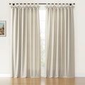 A pair of textured light beige tie-top curtains with decorative bow details hangs on a black rod covering a window with outdoor greenery in a room with a wooden floor and a small framed landscape painting on the left wall