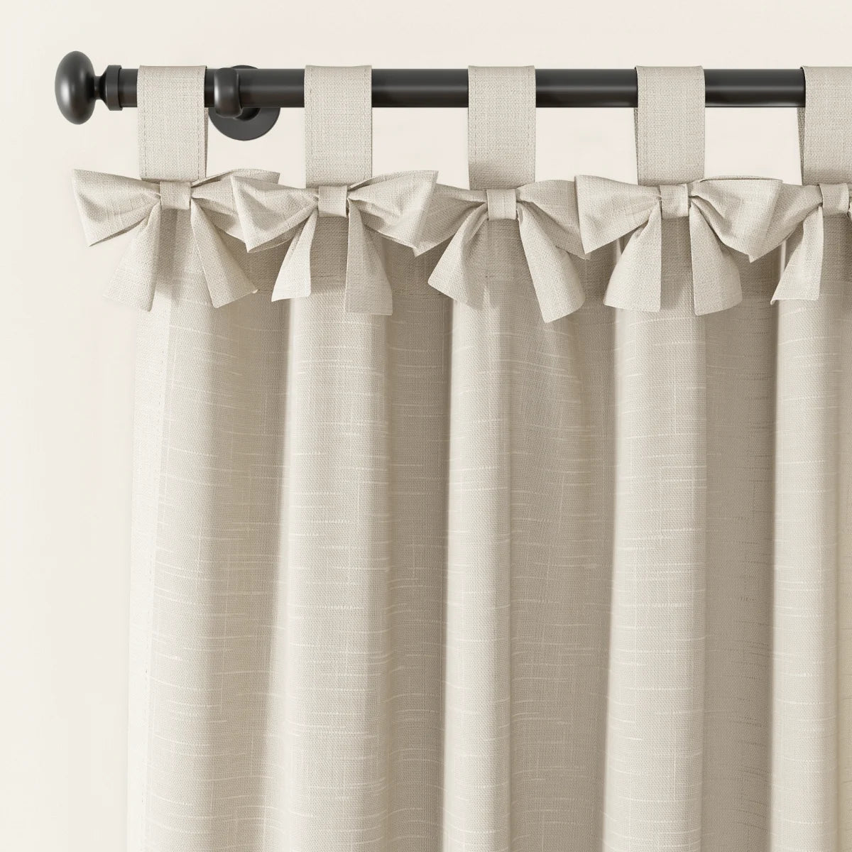 Beige linen-look curtain with decorative tie-top bows hanging from a dark curtain rod