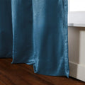 A rich teal blue curtain with a subtle sheen and visible weave elegantly drapes onto a dark wooden floor next to a white window sill revealing soft folds