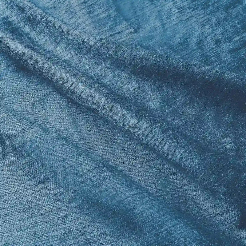 Photograph of deep teal blue textured fabric with soft folds revealing a subtle horizontal weave and luminous indigo hues