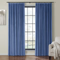 A pair of rich blue velvet pleated curtains frame a grid-patterned window in a home interior, flanked by an abstract gray tree art piece and a beige armchair with a textured throw