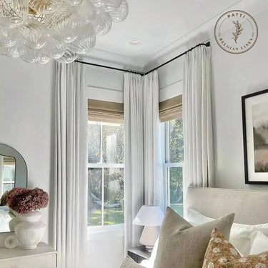 Patti Premium Belgian Linen Pleated Curtains - off white pleated curtains framing two corner bedroom windows beneath a crystal chandelier