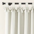 Off-white textured linen-look tie-top tab curtains with decorative bows hanging from a dark metal rod