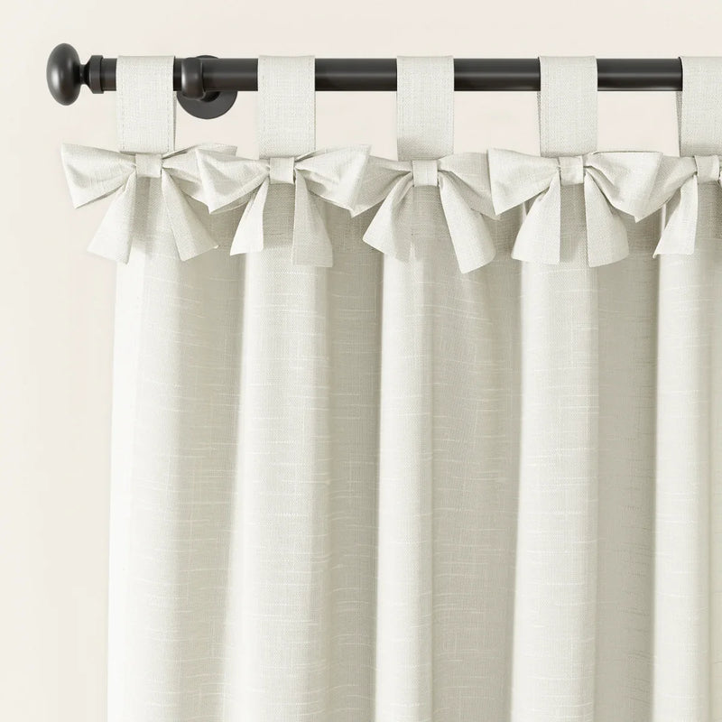 Off-white textured linen-look tie-top tab curtains with decorative bows hanging from a dark metal rod