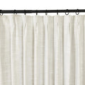 A close-up view of an off-white textured linen curtain with a pleated top hanging from a black metal rod with black rings