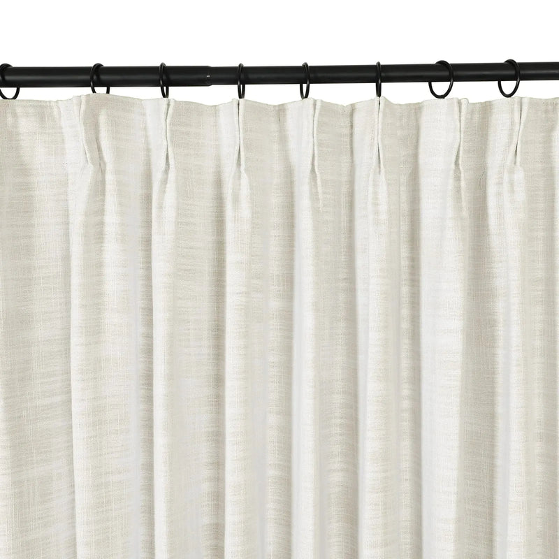 A close-up view of an off-white textured linen curtain with a pleated top hanging from a black metal rod with black rings