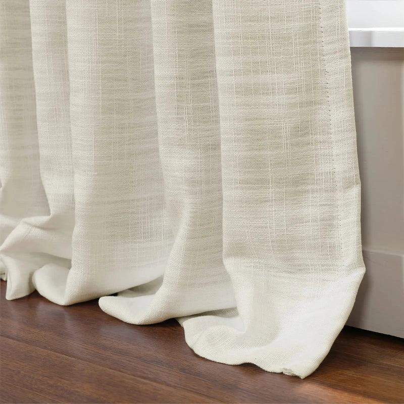 Close-up of natural ecru textured linen curtains with delicate weave, softly draped and puddling on a rich dark wood floor