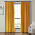 A cozy living room features rich mustard yellow velvet curtains framing a black grid-pane window, beside a light gray armchair with a white fringed throw blanket and minimalist monochromatic tree artwork on the wall