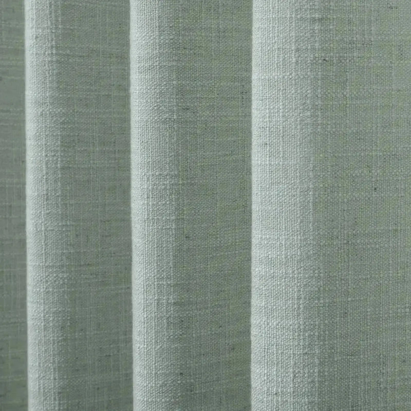 Textile featuring light sage green woven fabric with a distinct slubby texture arranged in soft vertical pleats