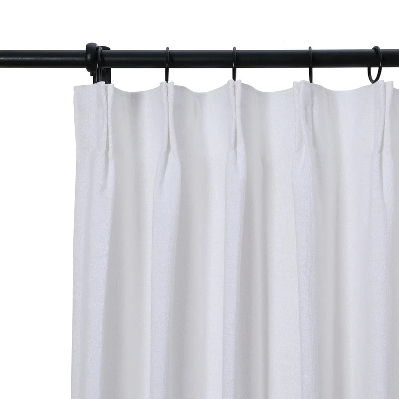 White textured fabric curtain with pleated top hanging from a black metal rod with black rings against a white background