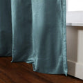 A richly textured teal curtain with a subtle sheen draped alongside a white window frame and extending to a dark brown wooden floor