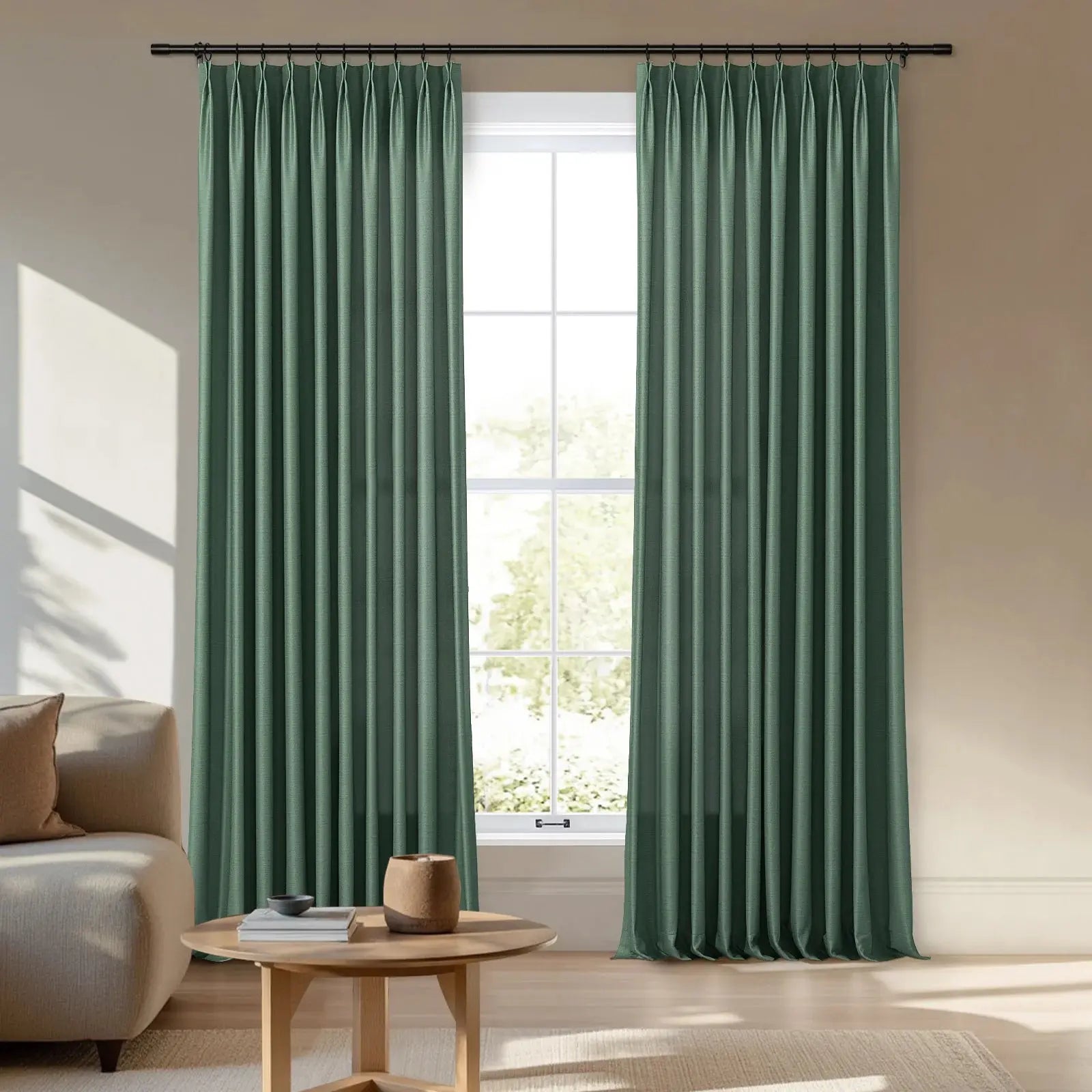 Deep sage green pleated curtains hanging from a black rod frame a sunlit window in a modern living room featuring a beige sofa and a round wooden coffee table
