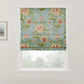 Fabric roman blind featuring a vintage floral pattern with large peach and yellow roses and green leaves on a teal blue background, partially covering a white window with a view of trees