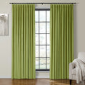Chartreuse green velvet curtains hanging on a black rod in an interior room, framing a large grid-paned window, with a cream armchair and a gray minimalist tree painting nearby