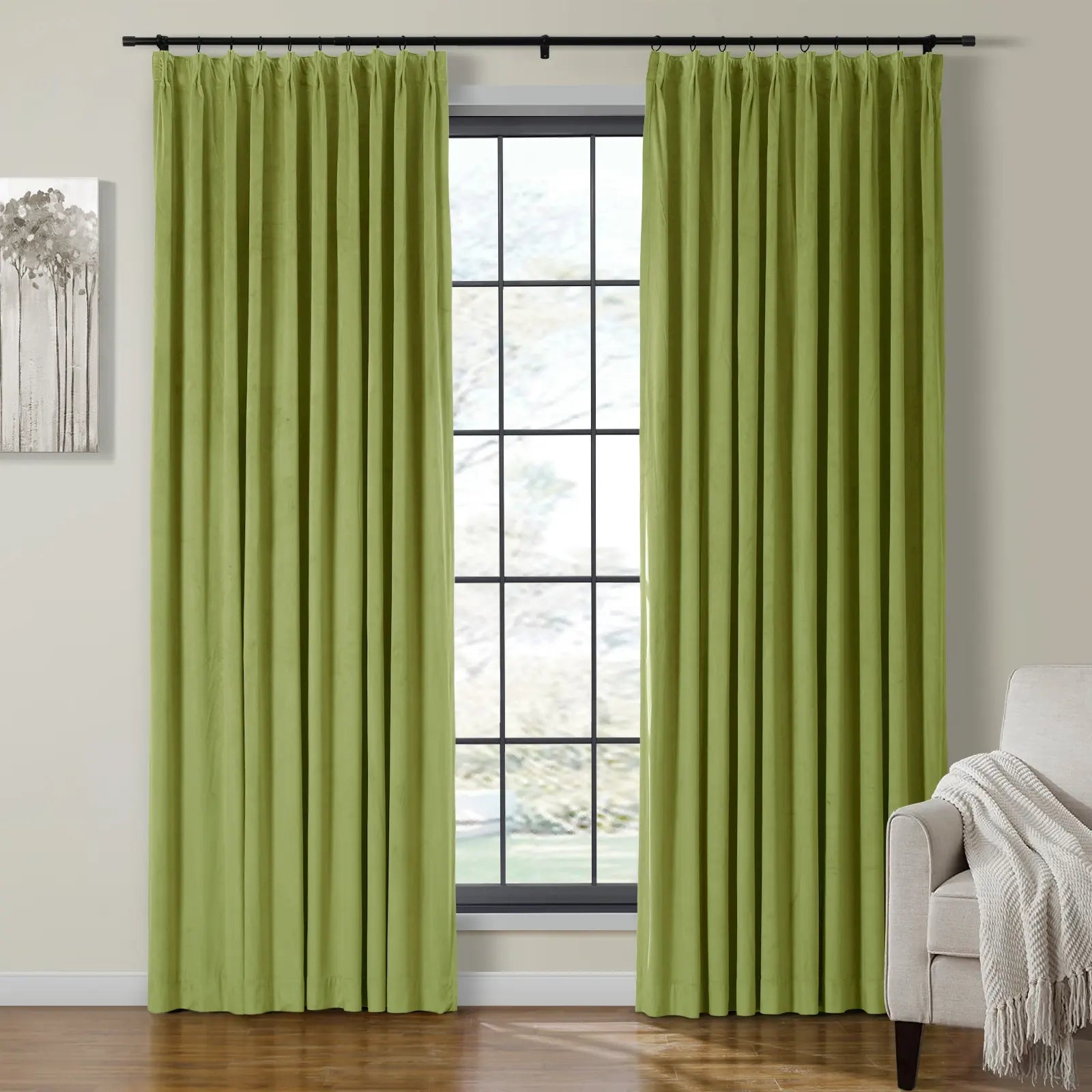 Chartreuse green velvet curtains hanging on a black rod in an interior room, framing a large grid-paned window, with a cream armchair and a gray minimalist tree painting nearby