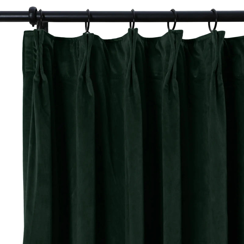 Forest green velvet curtain with lush pleated texture hanging from a black metal rod with rings