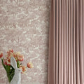 Photograph of an elegant interior featuring a clear vase with a white bunny figurine and vibrant pink and peach tulips against a light brown toile tree pattern wallpaper next to a dusty rose pleated curtain