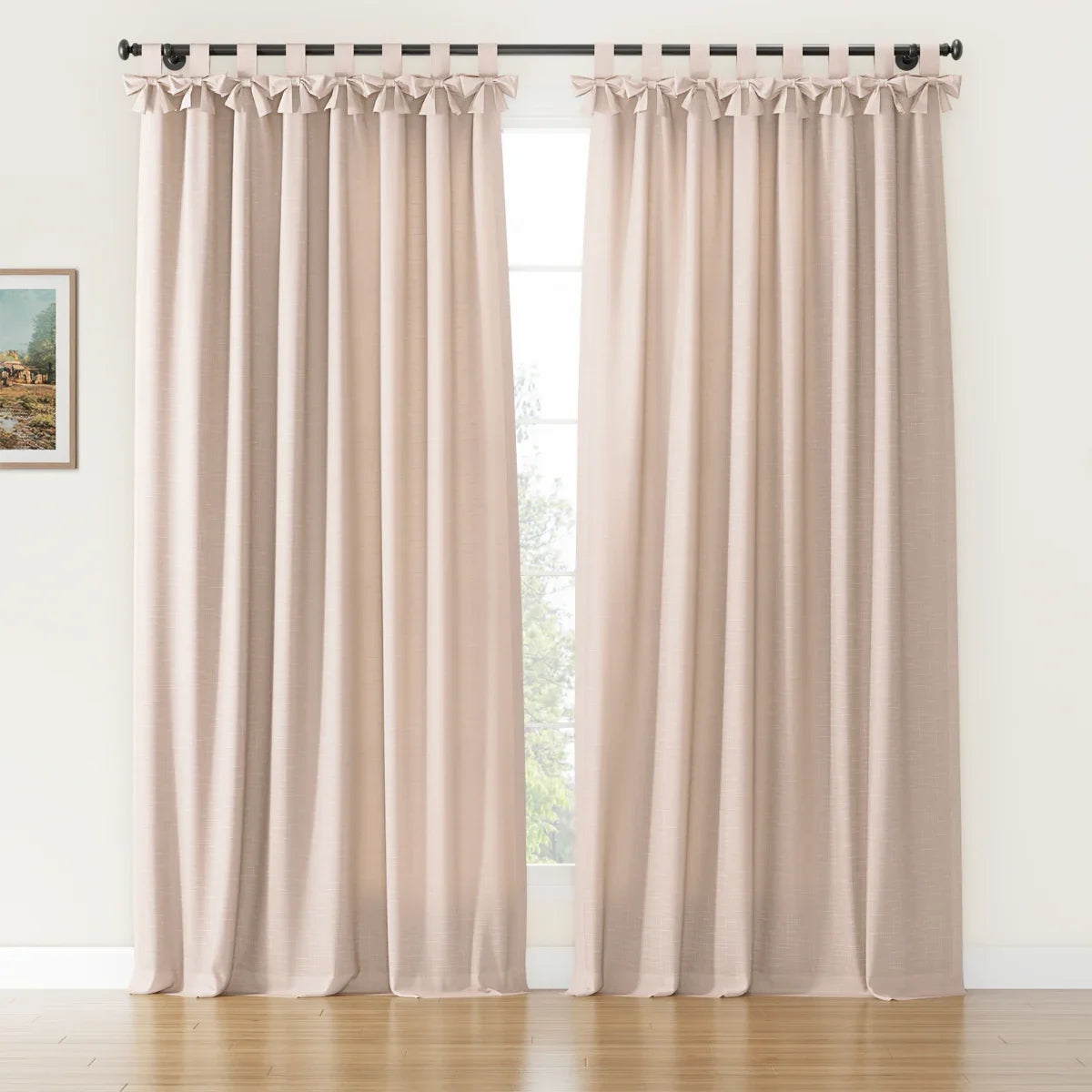 A pair of natural beige faux linen tab top curtains featuring decorative bows on a black rod in a room with a white wall, hardwood floor, and a small framed landscape painting