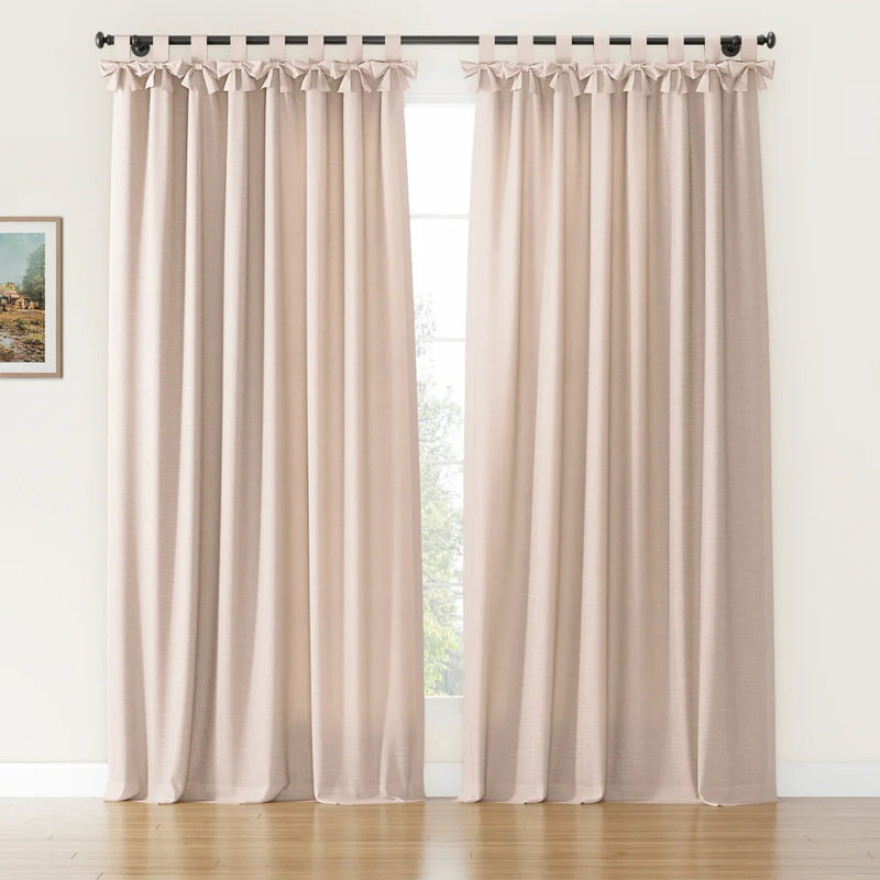 A pair of natural beige faux linen tab top curtains featuring decorative bows on a black rod in a room with a white wall, hardwood floor, and a small framed landscape painting
