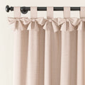 A blush pink textured curtain with decorative bow tie top tabs hanging on a black rod with a round finial