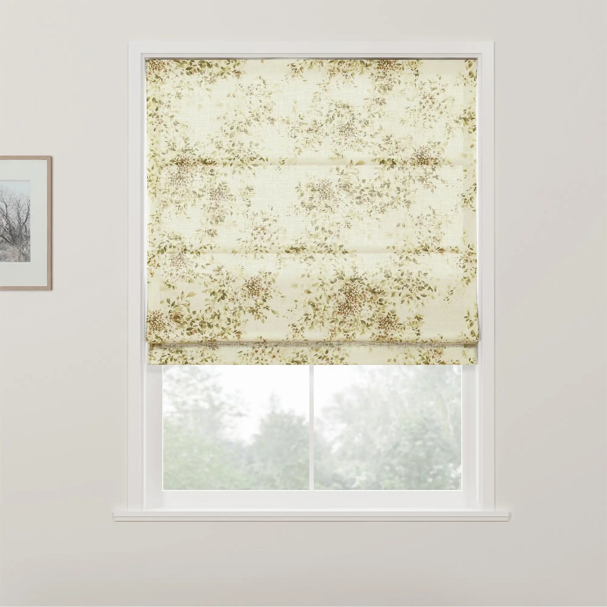 Photograph of an interior window featuring a textured cream Roman blind adorned with a subtle muted green and brown botanical pattern, partially raised to reveal a blurred view of lush green trees outside