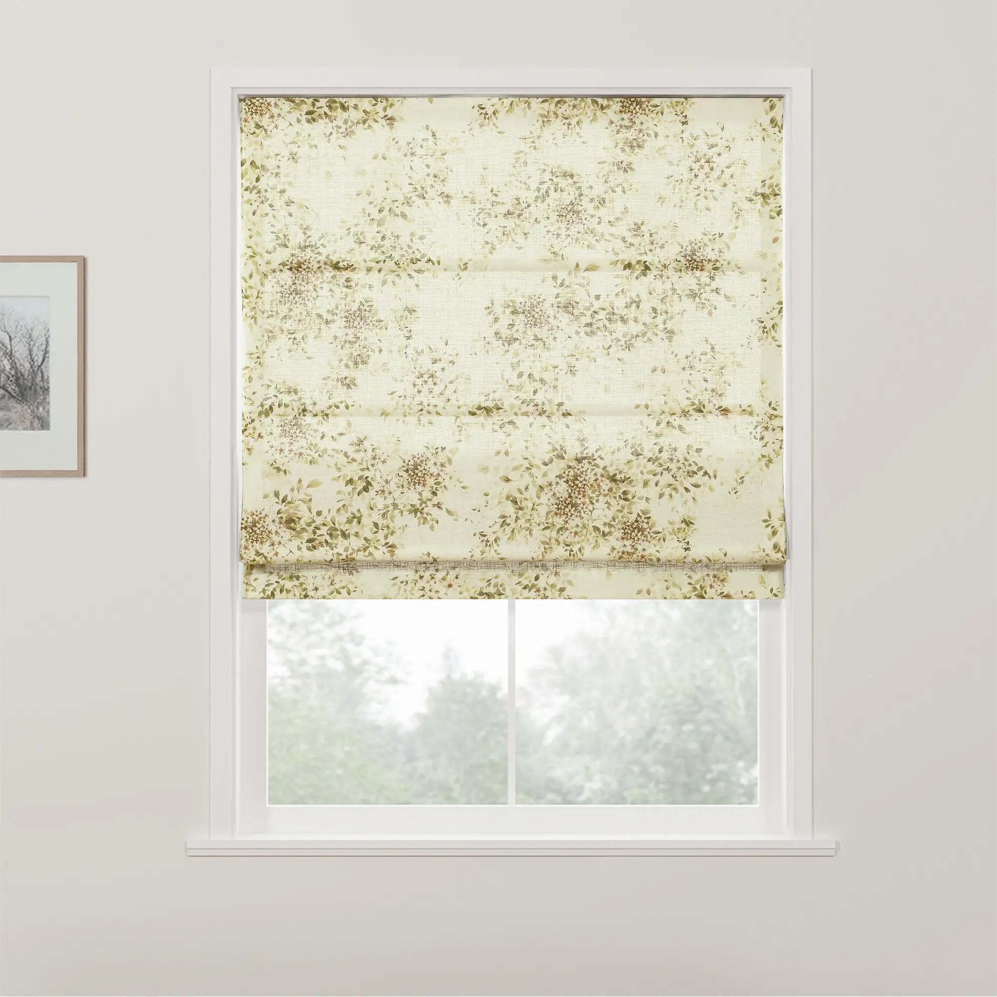 Photograph of an interior window featuring a textured cream Roman blind adorned with a subtle muted green and brown botanical pattern, partially raised to reveal a blurred view of lush green trees outside
