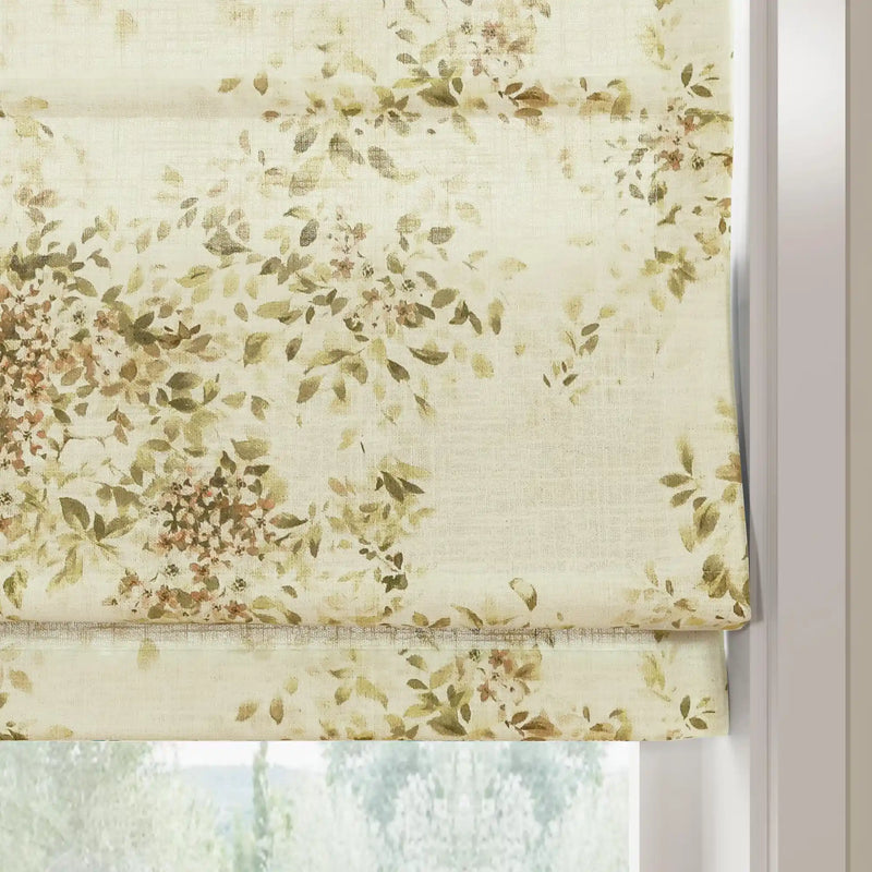 Fabric Roman blind with a watercolor botanical pattern featuring sage green leaves and soft brown blossoms on textured cream fabric partially covering a bright window