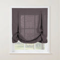 Dark gray linen balloon shade with decorative fabric button loops and a softly gathered bottom covering a white window frame revealing blurred green trees